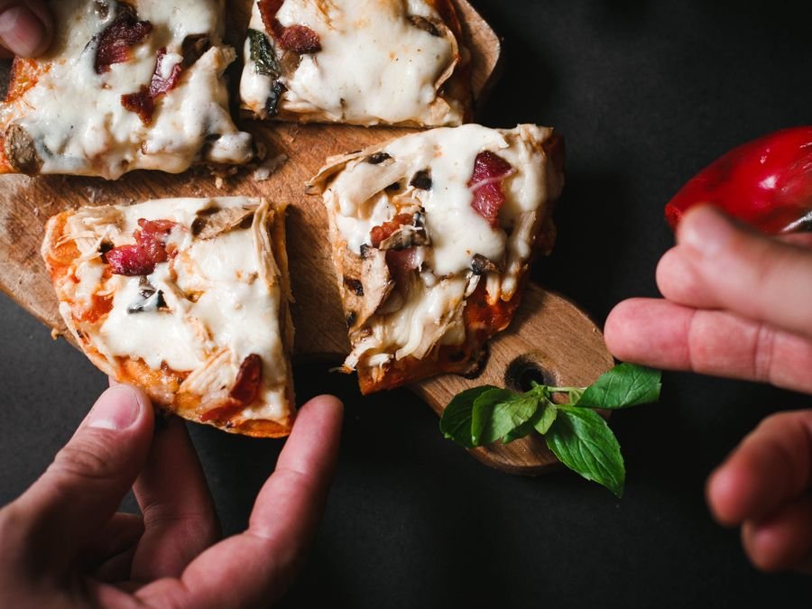 Manos sirviéndose porciones de pizza de muzzarella de una tabla